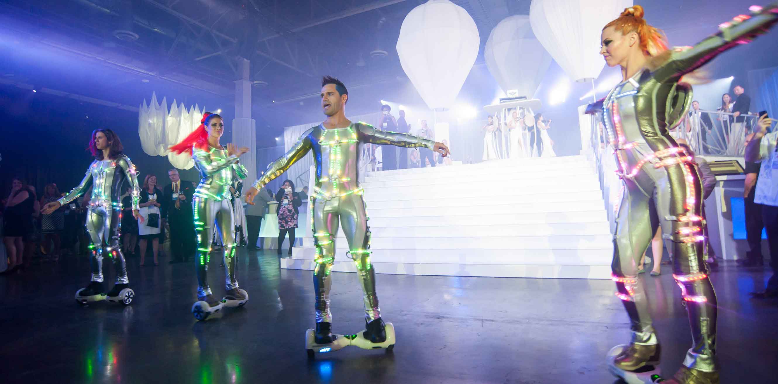 Performers in neon suits glide around the event on scooters